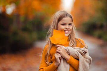 a teenage girl in a yellow sweater walks along a street outside the city against the backdrop of yellow trees. fun walk in autumn