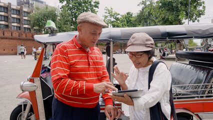 Two elderly Asian couples standing Next tuk tuk, holding tablet in hand, they are talking about tourist attractions, restaurants in Chiang Mai, In order be able travel many different places.