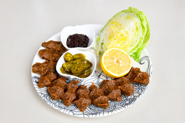 Cig kofte (raw meatball) with lettuce, tomato, pickle and lemon, hot Chee kofta. Turkish local raw food concept.Table scene of assorted take out or delivery foods. Doritoslu cig kofte durum.