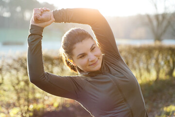 Beautiful sporty athletic young woman doing stretching exercises on a cold sunny morning in winter or autumn