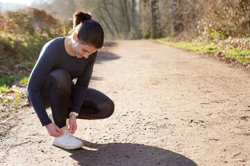 Sporty fit woman as a runner tying her shoes on a path on a sunny morning in winter or autumn