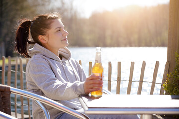 Cheerful woman on holiday, vacation or leisure drinking beer or lemonade from a bottle by the sea on a sunny day in summer