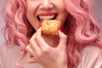 Woman with pink curly hair is eating baklava.