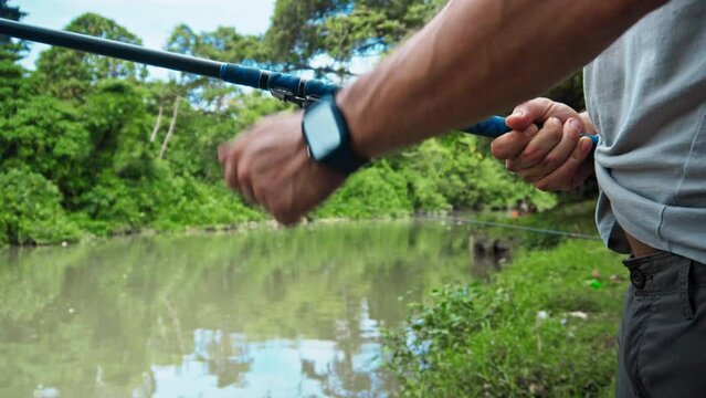young guy with a fishing rod in his hands, twists a reel and fishes in a river in a rainforest.