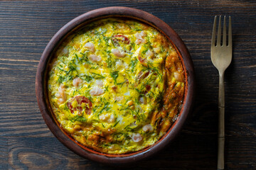 Ceramic bowl with vegetable frittata, simple food. Frittata with egg, tomato, pepper, onion, shrimps and cheese on wooden table, closeup, top view. Italian egg omelette