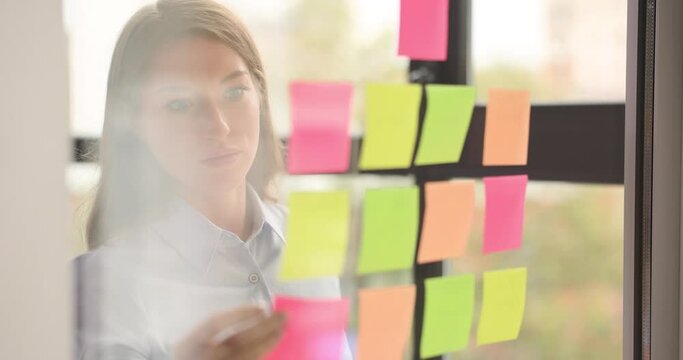 Seo or creative business manager sticking sticky notes to glass wall and whiteboard for sharing ideas in office