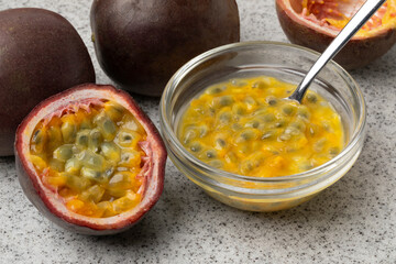 Halved fresh tropical passion fruit and a glass bowl with passion fruit juice and seeds close up 