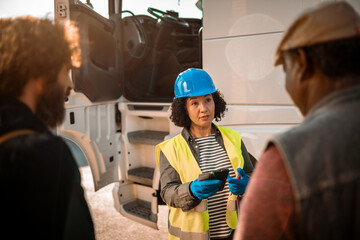 Woman logistic worker talking to truck drivers on parking lot