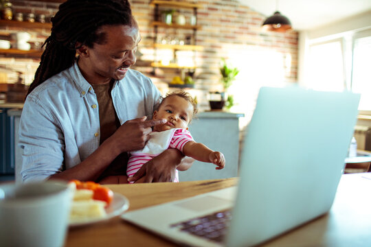 Young father playing with baby while working from home