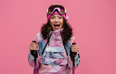 attractive smiling woman posing on pink background with skis in snow winter skiing sport suit