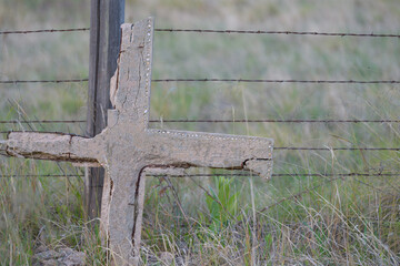 Old concrete cross grave marker leaning on barbed wire fence. selective focus on the grave marker