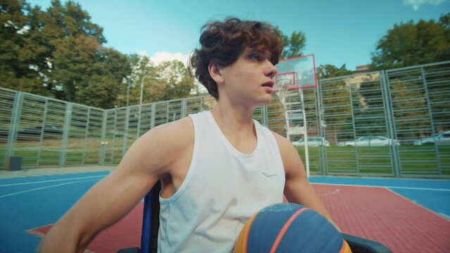 Close-up footage of nice Caucasian teenager moving in wheelchair on athletic field. Portrait of focused professional sportsman during pre-competition training. Morning time. Outdoor