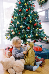 Fototapeta na wymiar Little girl sits on the floor near the Christmas tree and unpacks a gift