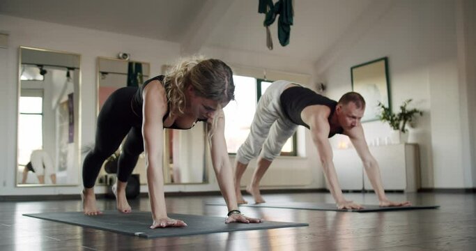Couple practicing yoga on exercise mats in studio. Man and woman exercising together indoors in morning. Healthy lifestyle, wellbeing, fitness exercise.