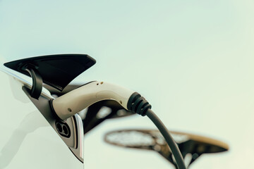 Closeup EV charger handle plugged in or connect to electric car, recharging EV car battery with...