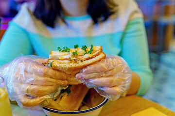 Hands of a girl in special signets holding a square sandwich with chicken, cheese and green onions