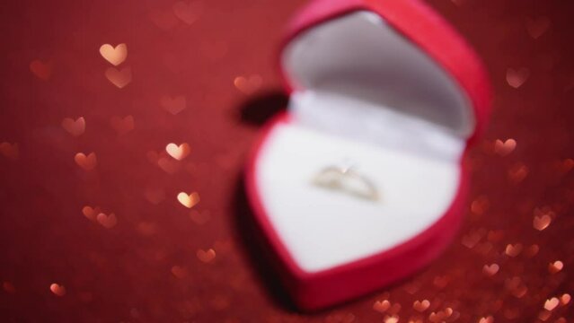 The engagement ring lies in an elegant box on red background with glitter coating. This background sparkles with rays light, creating enchanting sparkle that gives engagement ring even more radiance.