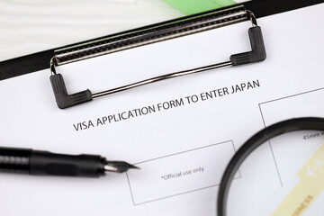 Visa application to enter Japan on A4 tablet lies on office table with pen and magnifying glass...