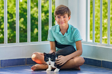 Handsome smiling teenager with black and white cat, portrait of a boy and his pet on green garden background 