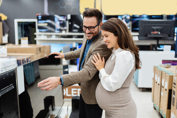 Beautiful and happy middle age couple buying consumer tech products in modern home appliances store. They are choosing home theater and TV devices. People and consumerism concept. - obrazy, fototapety, plakaty