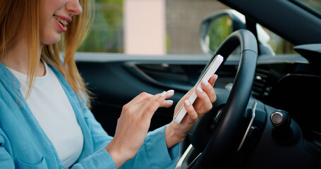 Close up. Beautiful young woman sitting in a car on drivers seat and using smartphone. Driver checking email chats reading news. Driver writing message SMS vehicle on social network chats cellphone.