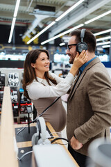 Beautiful and happy middle age couple buying consumer tech products in modern home electronics store. They are choosing high quality hi-fi audio speakers and audiophiles headphones.
