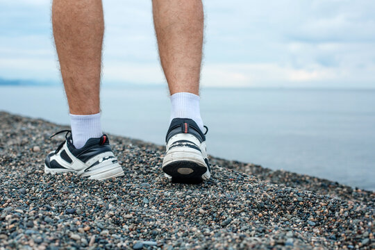 Close-up fashion image of a man walking alone on a pebble beach, wearing stylish shorts and sneakers