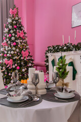 Table setting, silver wine glasses. Christmas tree in pink colors with a white decorative fireplace and candlesticks.