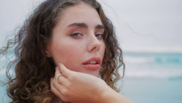 Close up gorgeous beauty model look in camera at beach. Skin care cosmetics product concept. Professional fashion model 4K. Portrait of young curly brunette woman with perfect skin and light blue eyes