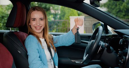 Woman sitting in car holds keys with delighted and show keys wants to buy new automobile in car. Attractive girl holding a key from her new car, smiling and singing.