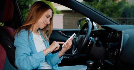 Young woman is sitting in the driver's seat using a touch display screen multimedia device in...