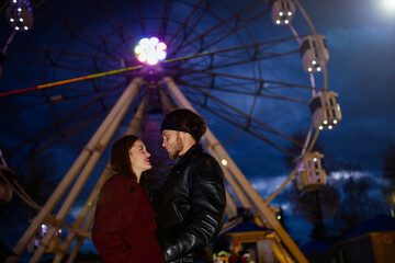 couple in love in an amusement park near a ferris wheel on a date in cold weather. The concept of love and joy in relationships.
