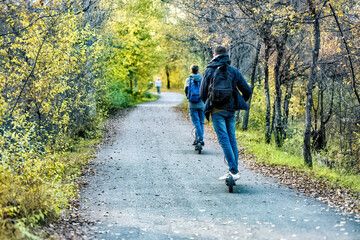 A young men are riding on the electric scooter in a park.