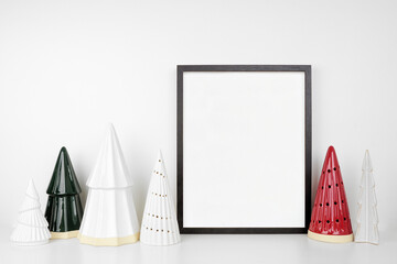 Christmas mock up with black frame and tree decor. Portrait frame on a white shelf against a white...