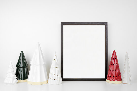 Christmas mock up with black frame and tree decor. Portrait frame on a white shelf against a white wall. Copy space.