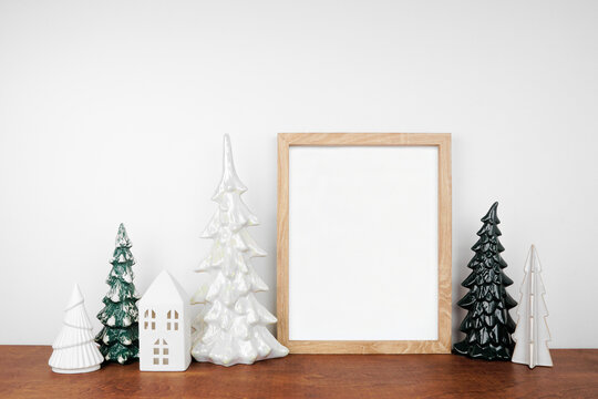 Christmas mock up with wooden frame, trees and white house decor. Portrait frame on a wood shelf against a white wall. Copy space.