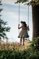 A small and beautiful girl in a dress is swinging on a swing.