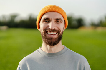 Handsome bearded middle aged man wearing stylish casual yellow hat, looking at camera in park