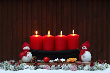 Vierter Advent: Adventsdekoration mit roten Kerzen, Weihnachtsschmuck und Dekofiguren im Schnee.