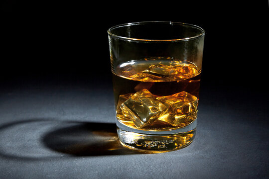 Glass of whiskey with ice on black stone table