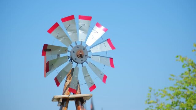A vintage windmill spins with the wind on a blue sky. Rural scene