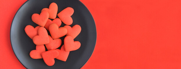 Red heart shaped cookies on the black plate on the red background. Top view. Copy space.