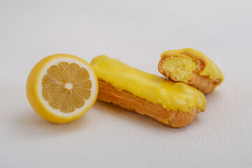 Half of a cut lemon next to an eclair in yellow glaze and sweet cream on a white background.