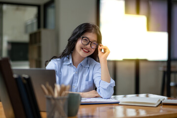 Smart Asian businesswoman sitting happily working at the table and touching her glasses.