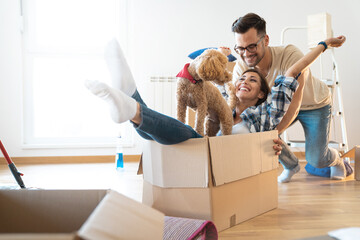 Cheerful young couple being silly having fun while unpacking boxes at new home, together with their...