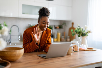 Kind smiling businesswoman waving hand looking at laptop during virtual video conference call in home office.