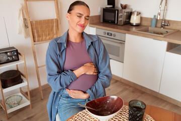 Pregnant woman in kitchen, clutching belly after overeating