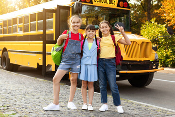 Portrait of three multiethnic preteen girls standing outside near yellow school bus