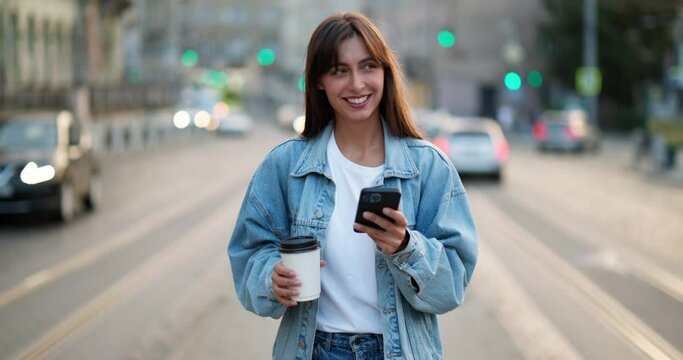 Woman in jeans jacket walking in the crowded street, using smartphone