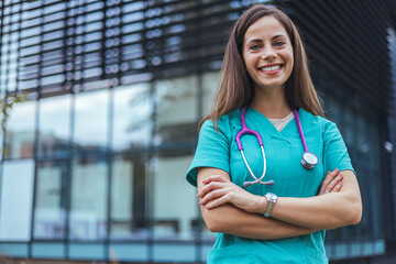 Portrait of happy young female nurse with folded arms standing in hospital. Confident doctor woman in uniform and stethoscope looking at camera with copy space. 